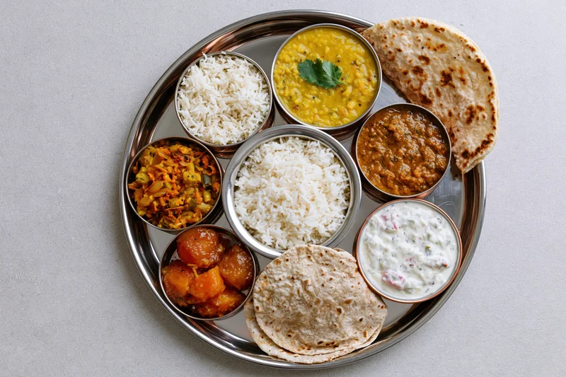 Indian thali meal with rice, dal, curry, roti and raita arranged on a steel plate