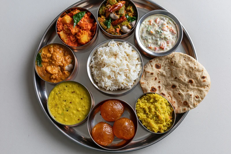 Indian thali meal with rice, curries, dal, roti and sweets arranged on a steel plate