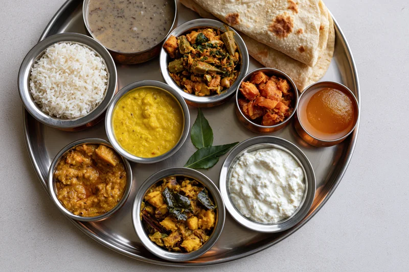 Indian thali meal with rice, curries, dal, yogurt, pickle, and roti arranged on a steel tray