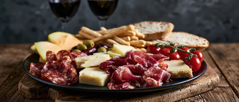 Italian charcuterie platter with cured meats, cheeses, bread, and wine on a rustic wooden table