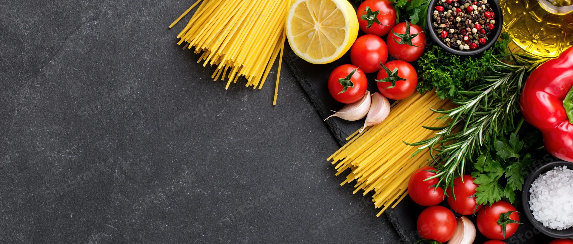 Italian cooking ingredients arranged along the right edge of a dark slate surface with copyspace on the left