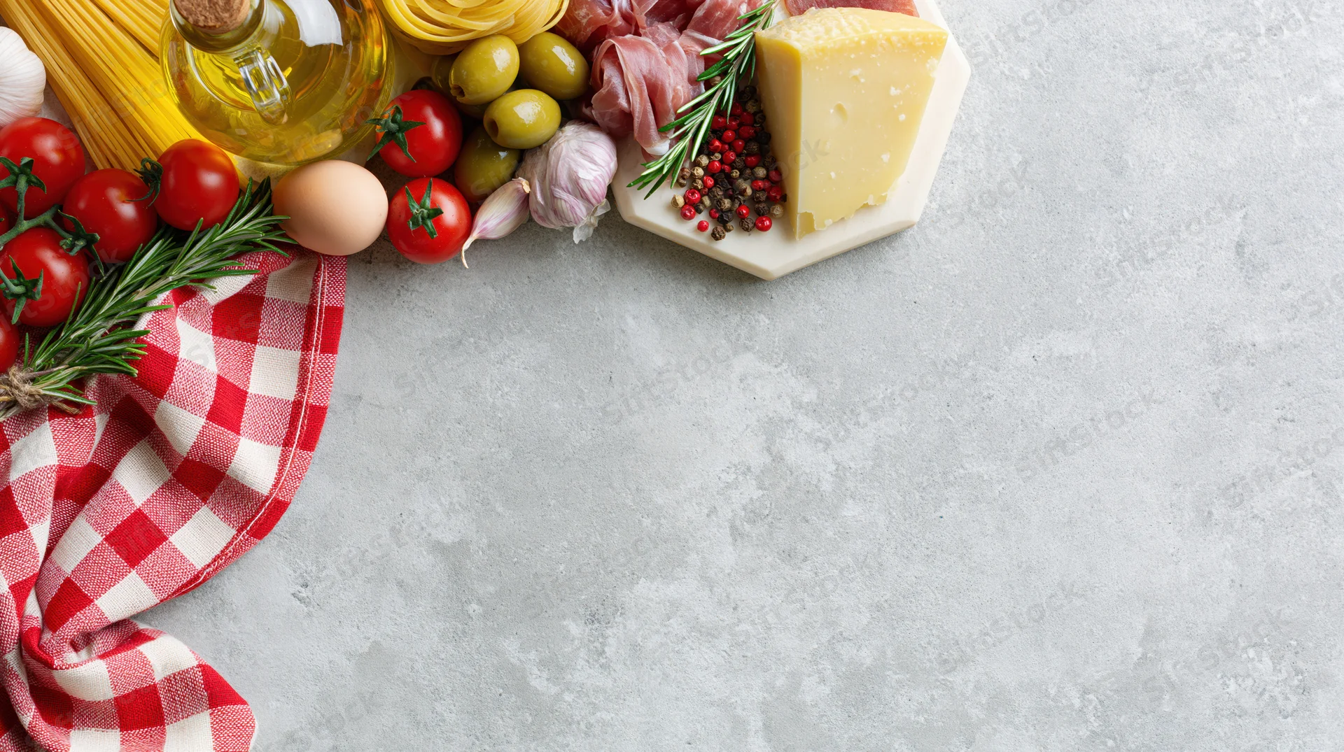 Italian cooking ingredients arranged along the top-left border on a gray countertop with copyspace