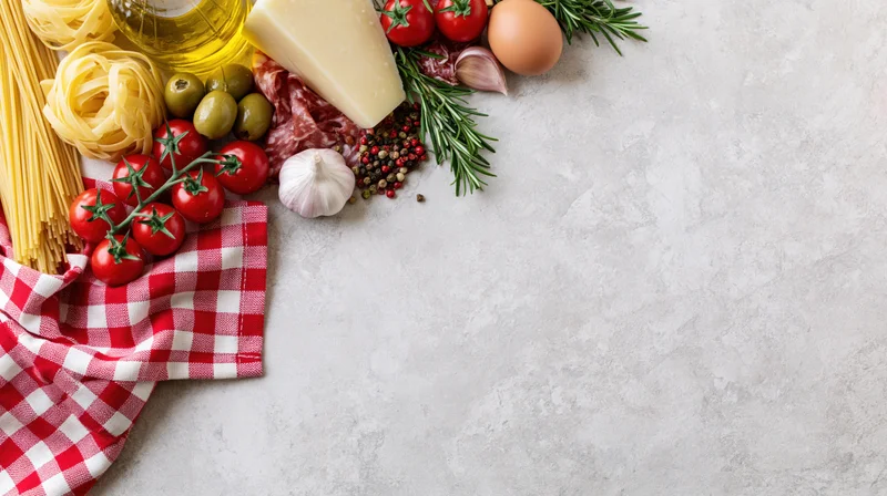 Italian cooking ingredients arranged along the top-left border on a white countertop with copyspace