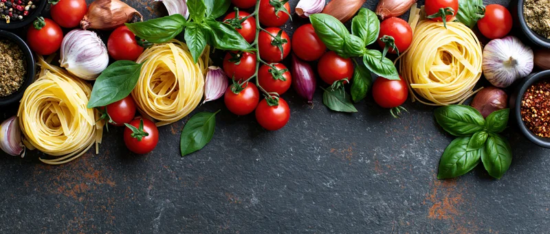 Italian cooking ingredients arranged along the top edge of a dark slate surface with copyspace below