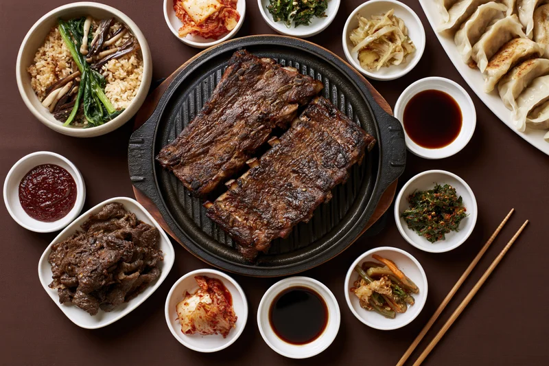 Overhead view of korean barbecue spread with grilled galbi ribs and side dishes on table