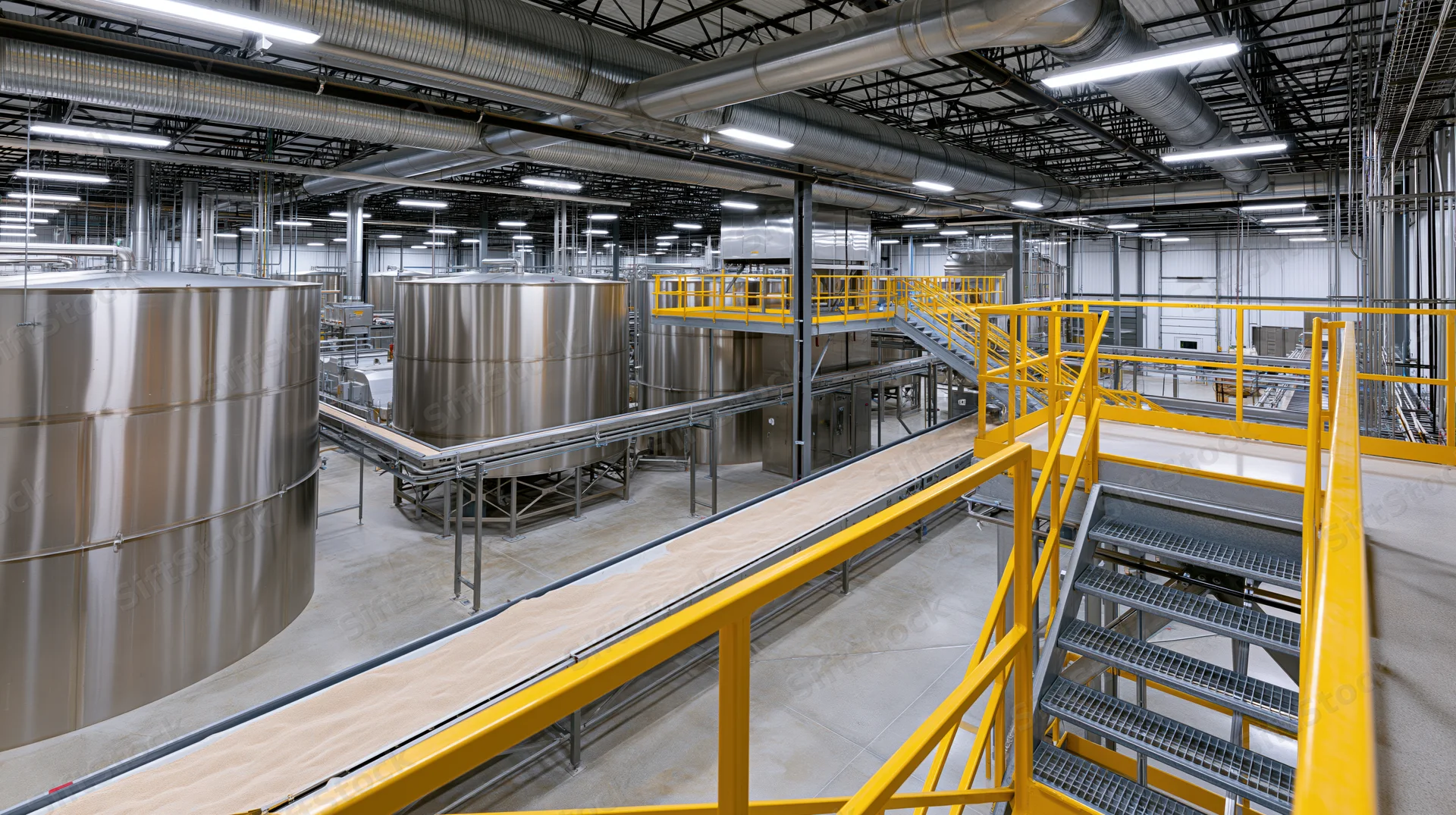 Interior of a large-scale food processing facility with stainless steel tanks and yellow safety railings