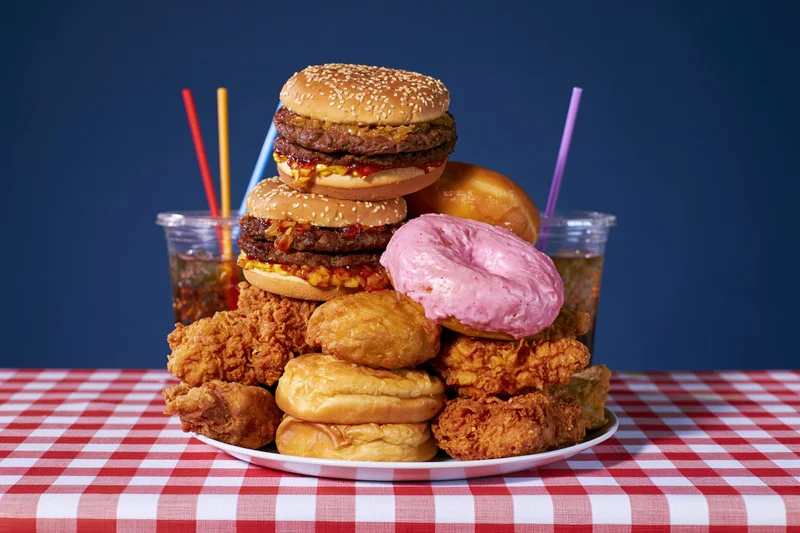 Pile of burgers, donuts, fried chicken and soda on a red and white checkered tablecloth