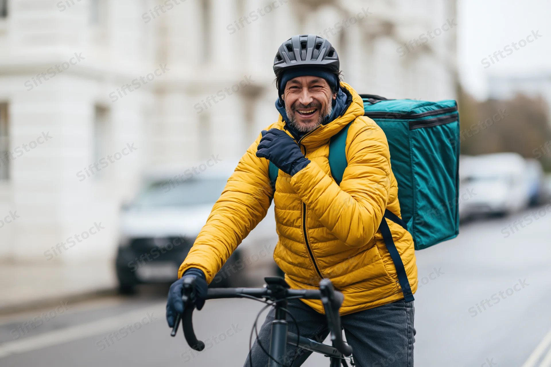 Smiling male delivery cyclist on bicycle in city street wearing yellow jacket and helmet with teal backpack