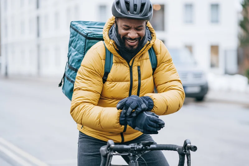 Man laughing while adjusting gloves on bicycle in winter city street