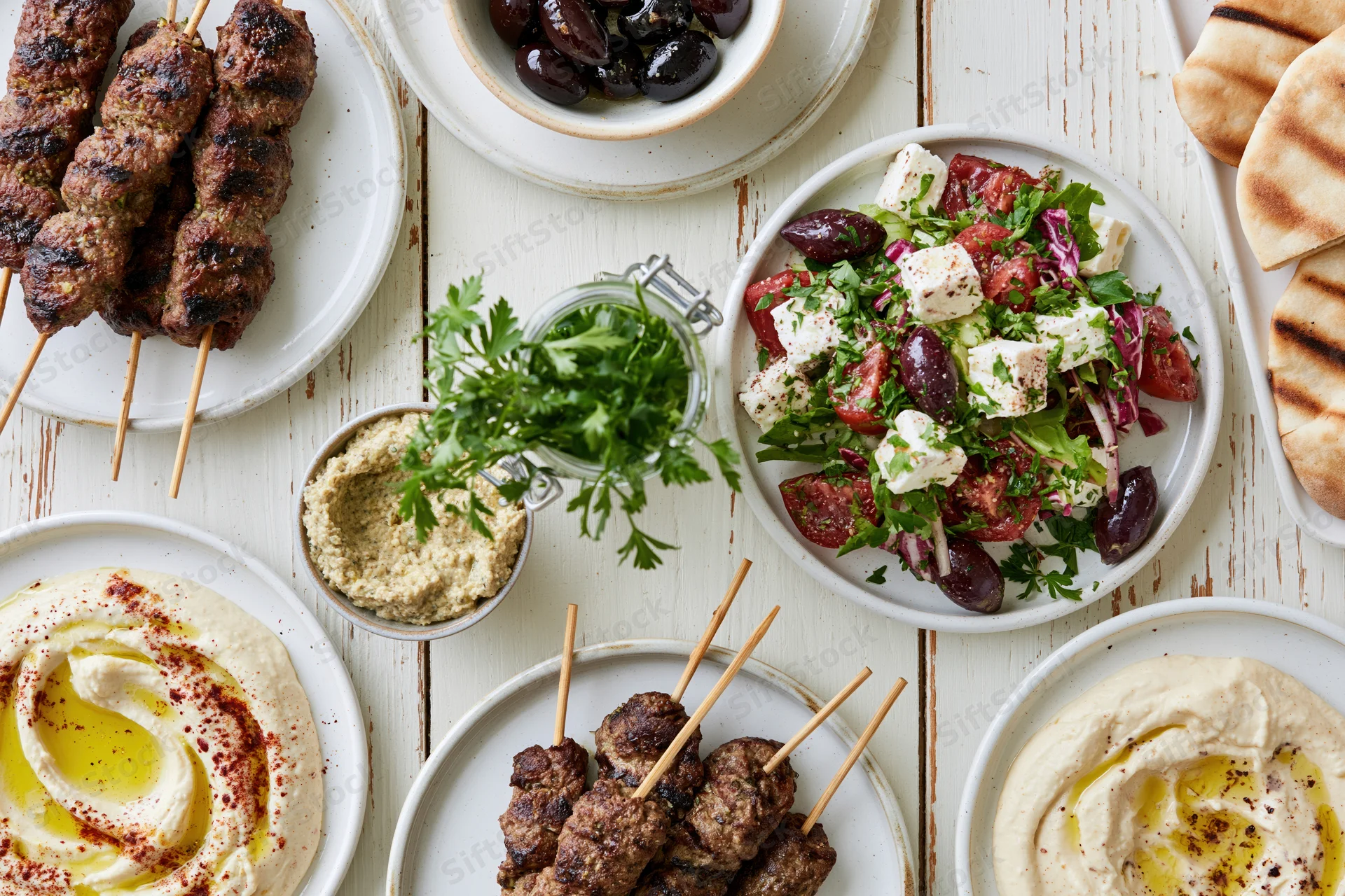 Mediterranean mezze spread with hummus, kebabs, salad and pita on a white wooden table