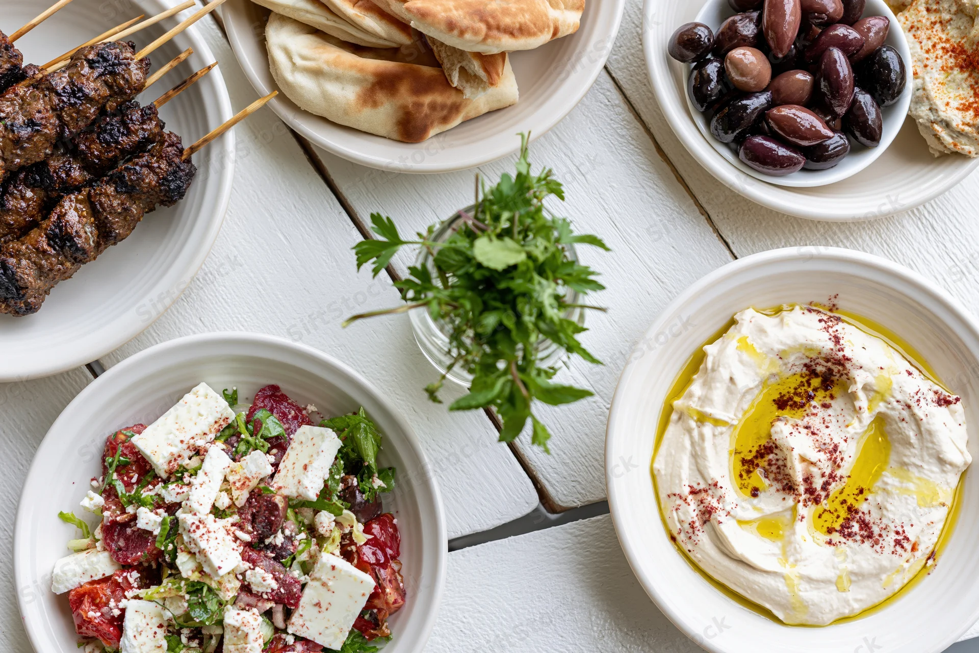 Mediterranean mezze spread with hummus, pita, olives and grilled kebabs on a white wooden table