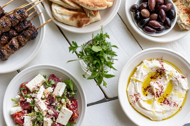 Mediterranean mezze spread with hummus, pita, olives and grilled kebabs on a white wooden table