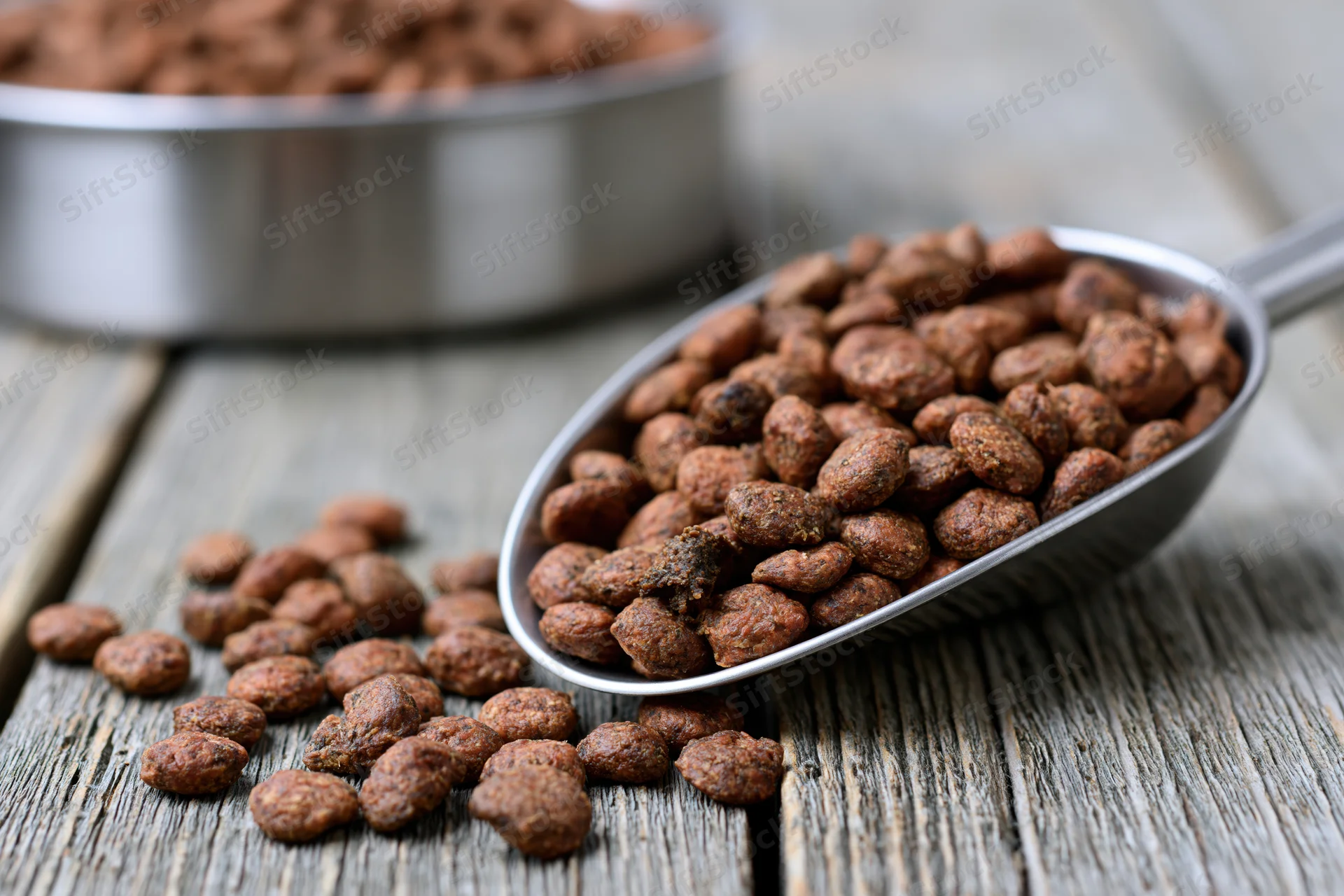 Metal scoop overflowing with dry pet kibble scattered on wooden table