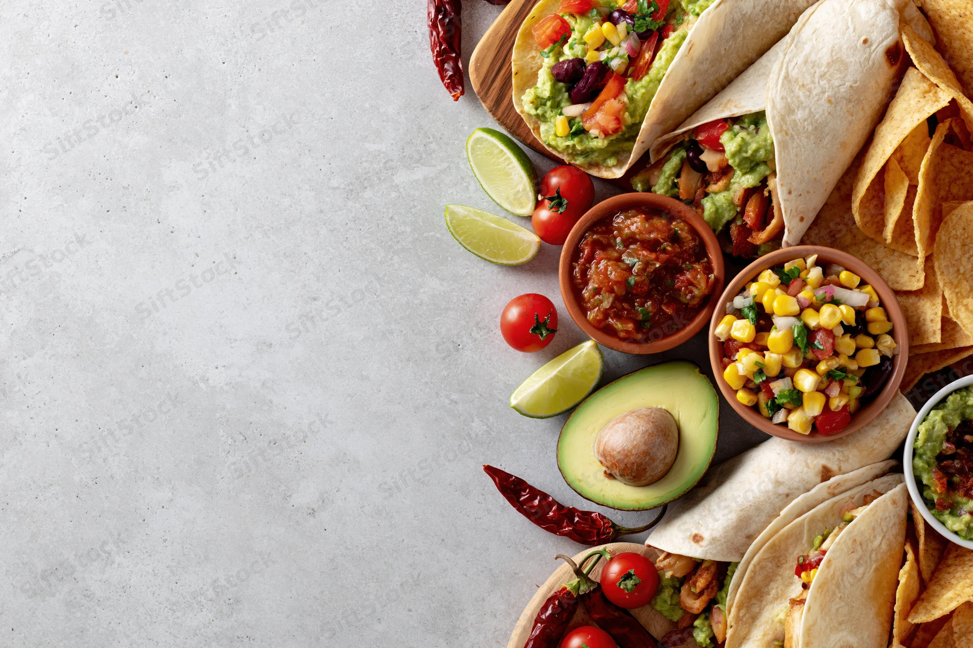 Mexican food spread with tacos, guacamole, salsa, and chips arranged along the right edge of a white surface
