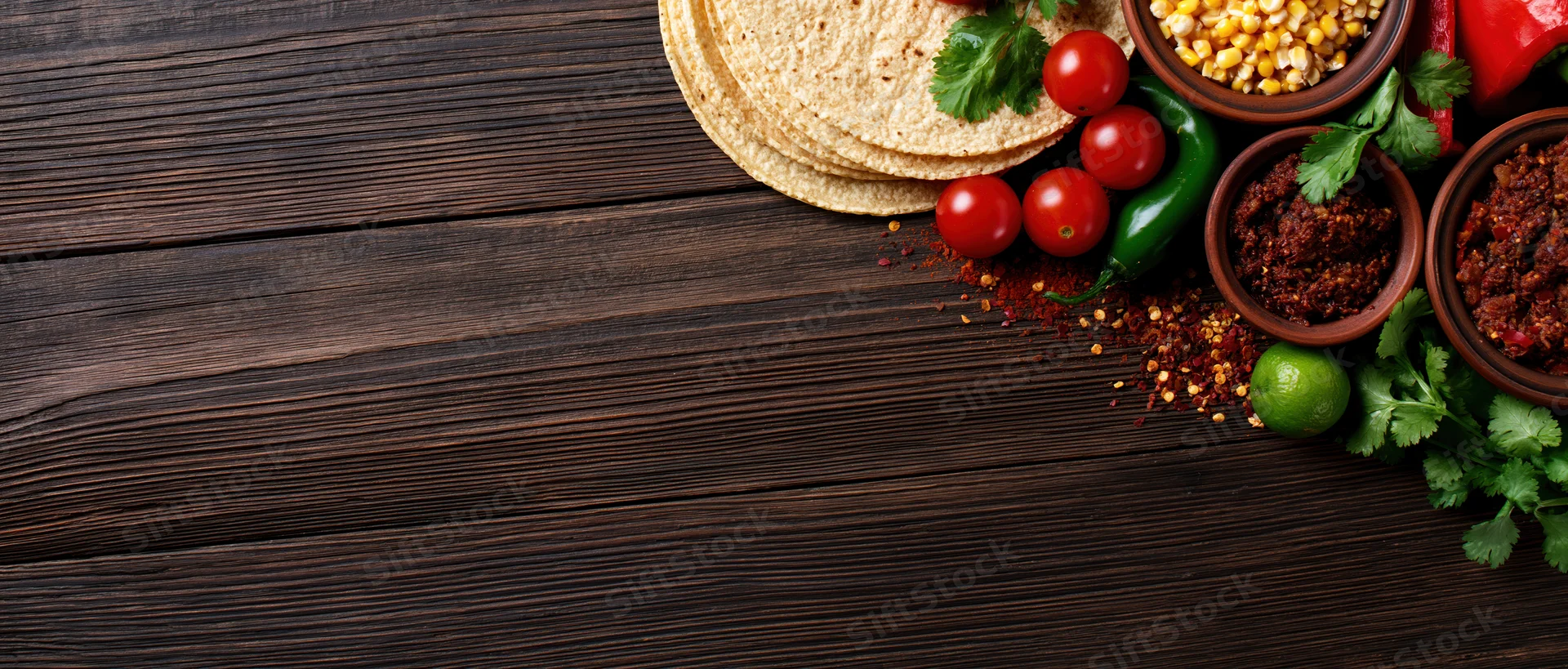 Mexican taco ingredients arranged along the right edge of a dark wooden table with copyspace on the left