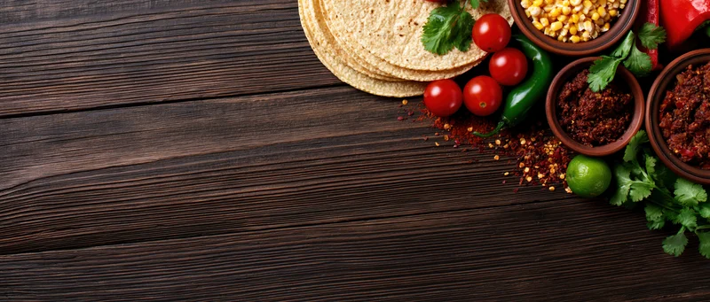 Mexican taco ingredients arranged along the right edge of a dark wooden table with copyspace on the left