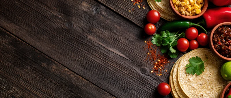 Mexican taco ingredients arranged along the right edge of a dark wooden table