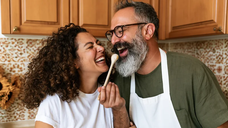 Laughing couple in kitchen sharing wooden spoon while cooking together
