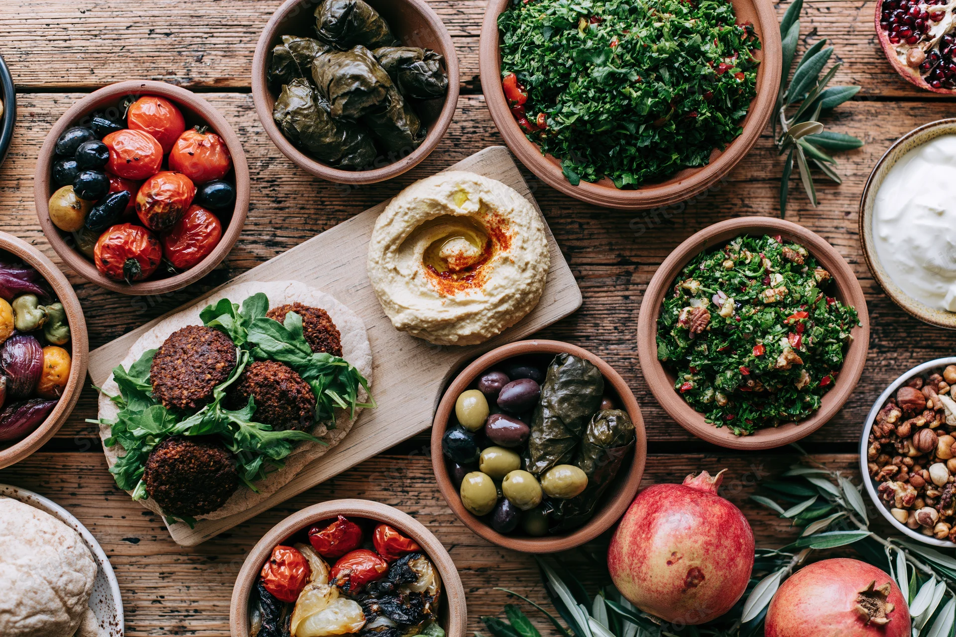 Middle eastern mezze spread with hummus, falafel, tabbouleh, olives, pomegranate, and vegetables arranged on a rustic wooden table