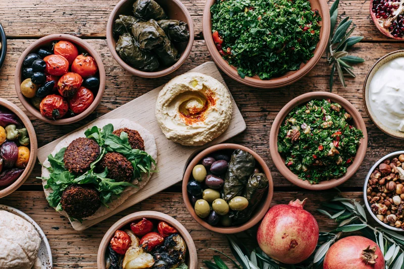 Middle eastern mezze spread with hummus, falafel, tabbouleh, olives, pomegranate, and vegetables arranged on a rustic wooden table