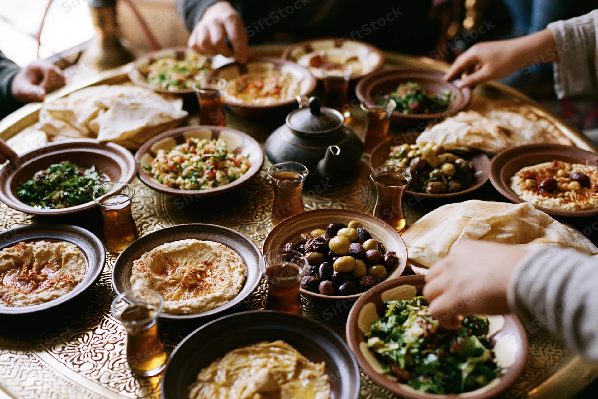 Middle eastern mezze spread on ornate brass tray with hands serving food and drinks