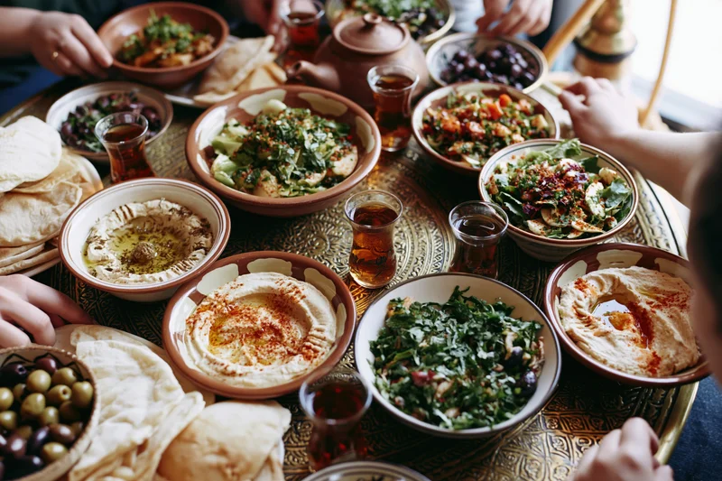 Middle eastern mezze spread on ornate brass tray with hands reaching for food and drinks