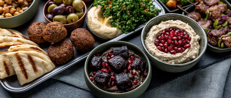 Middle eastern mezze spread with hummus, falafel, pita, olives and pomegranate on dark slate surface