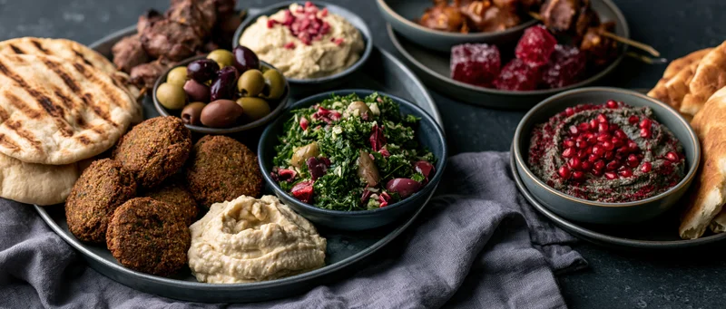 Middle eastern mezze spread with hummus, falafel, pita, tabbouleh, olives and baba ghanoush on dark slate surface