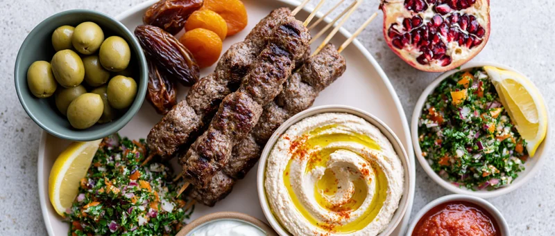 Middle eastern mezze platter with grilled meat skewers, hummus, tabbouleh, olives and pomegranate on stone surface