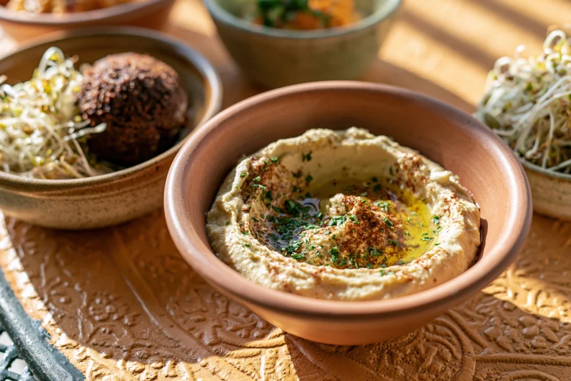 Hummus in a clay bowl with garnishes on a decorated metal tray surrounded by mezze dishes