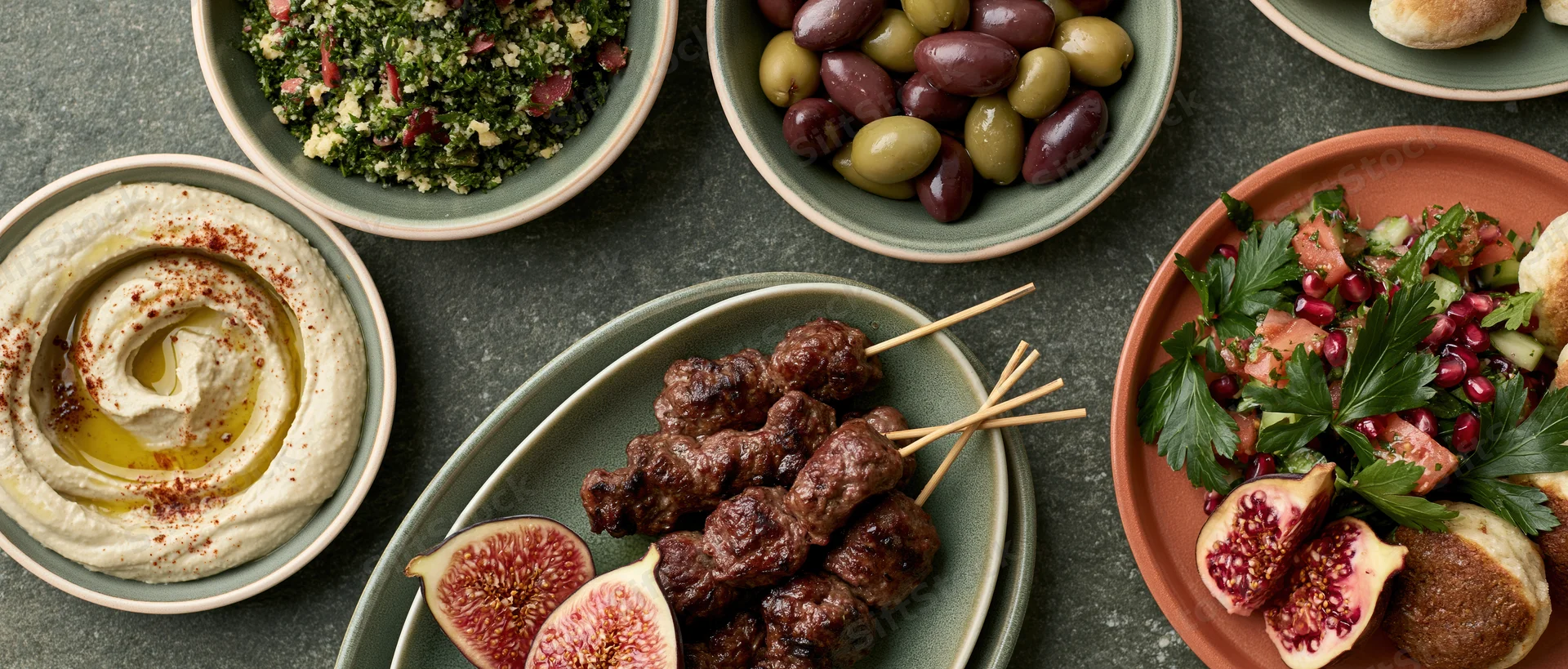 Overhead view of a middle eastern mezze spread with hummus, olives, kebabs, figs and salad on ceramic plates and bowls