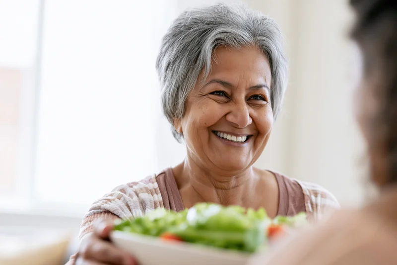 Senior southasian woman smiling while serving a salad at home
