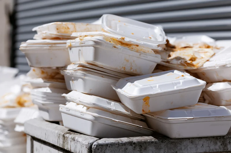 Pile of used styrofoam takeout containers stacked on a concrete ledge outdoors