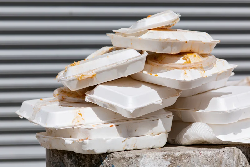 Pile of used styrofoam takeout containers stacked on concrete block outdoors