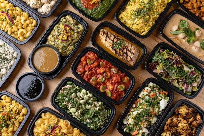 Overhead view of multiple prepacked meals in black containers arranged on a wooden table