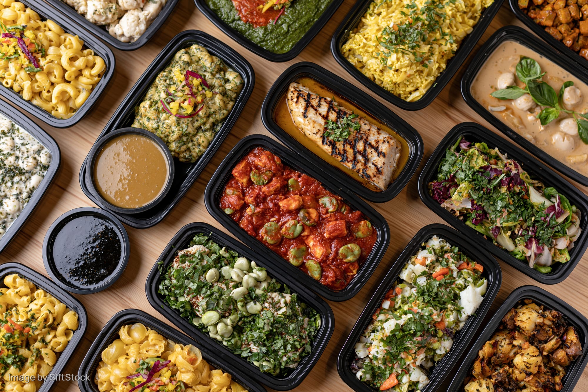 Overhead view of multiple prepacked meals in black containers arranged on a wooden table