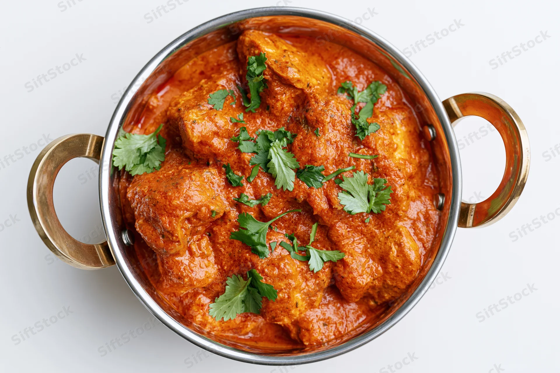 Butter chicken curry in a stainless steel balti bowl with cilantro garnish, overhead view on white background