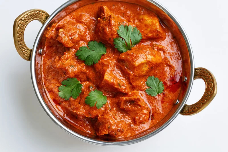 Butter chicken curry in a metal bowl with cilantro garnish, overhead close-up on white background