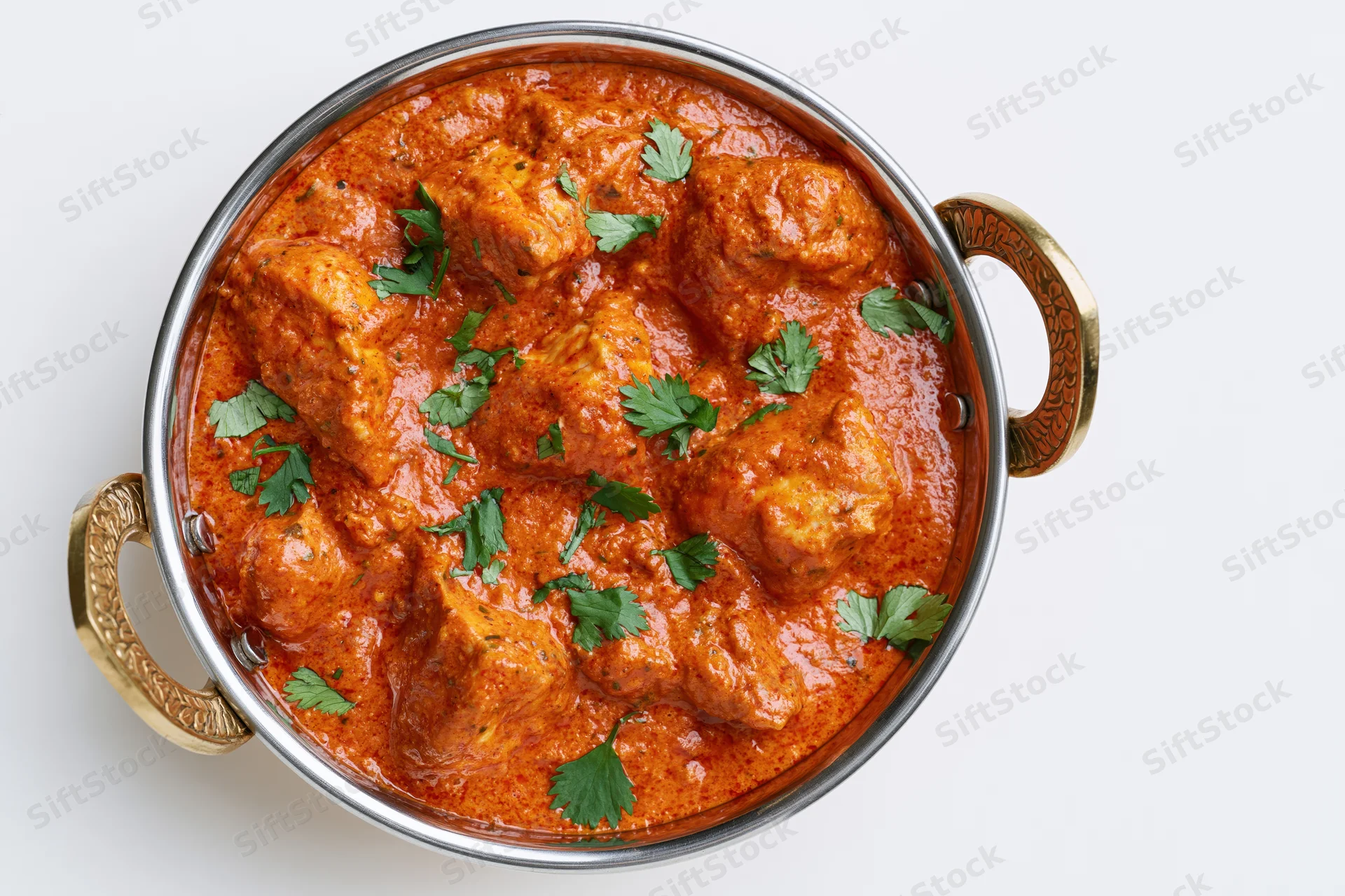 Butter chicken curry in a stainless steel balti dish with cilantro garnish, overhead view on white background