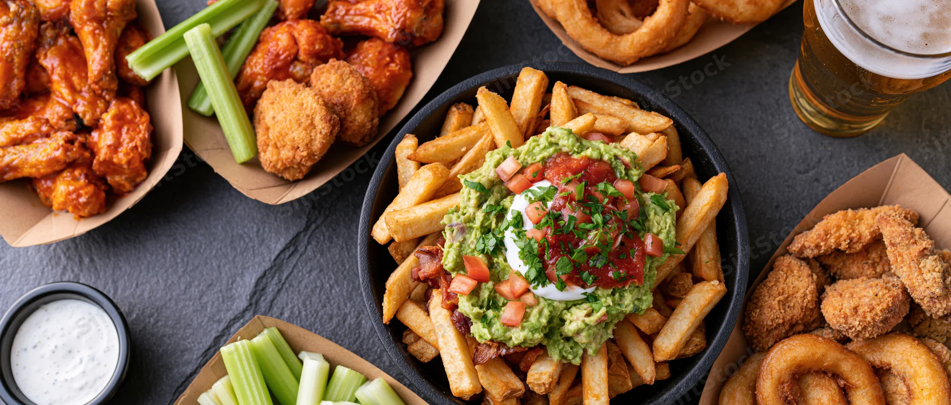 Overhead flat-lay of american bar food spread on dark slate surface