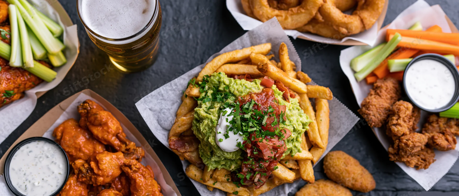 Overhead flat-lay of american bar food spread on dark slate surface