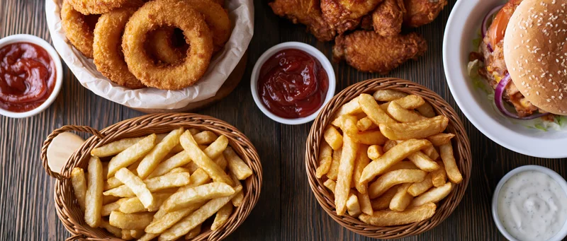 Overhead flat-lay of american fast food including burger, fries, onion rings and chicken wings on dark wooden table