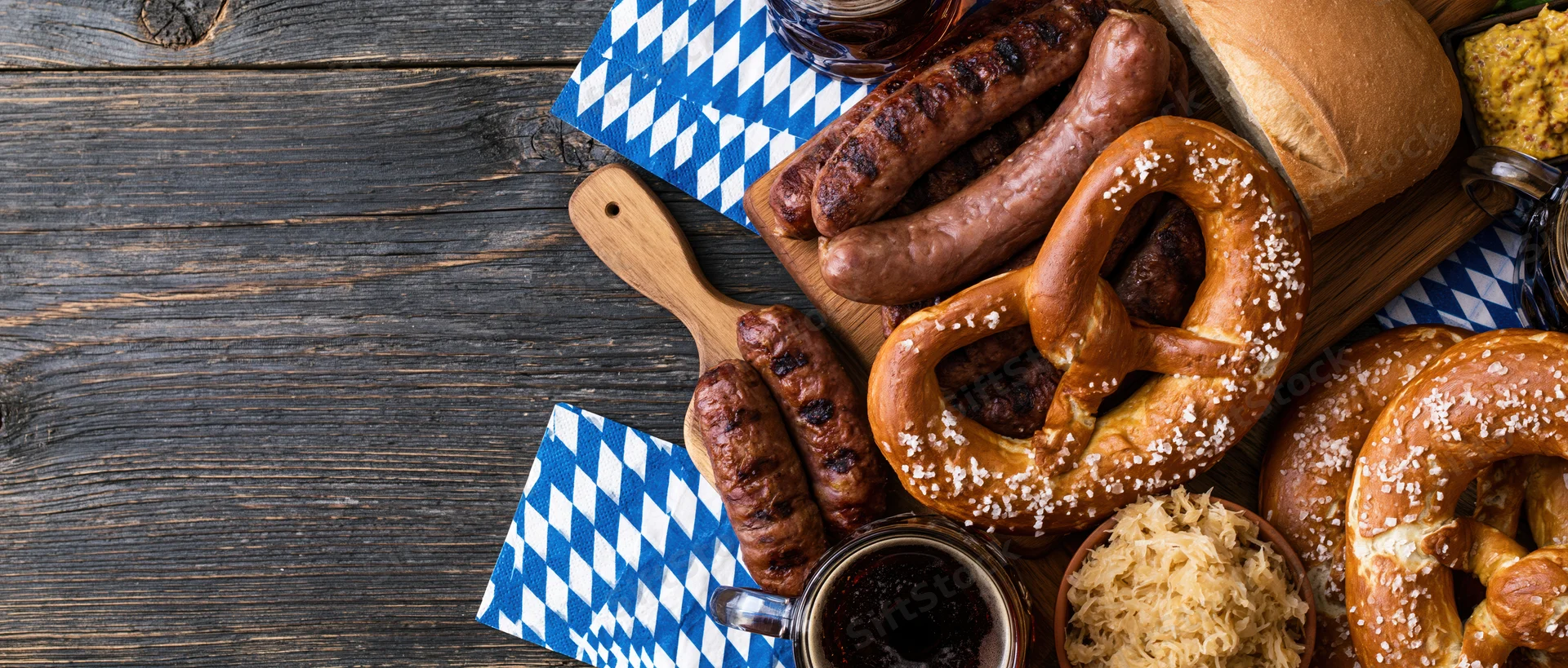 Traditional oktoberfest food spread with sausages, pretzels, and beer on a dark wooden table