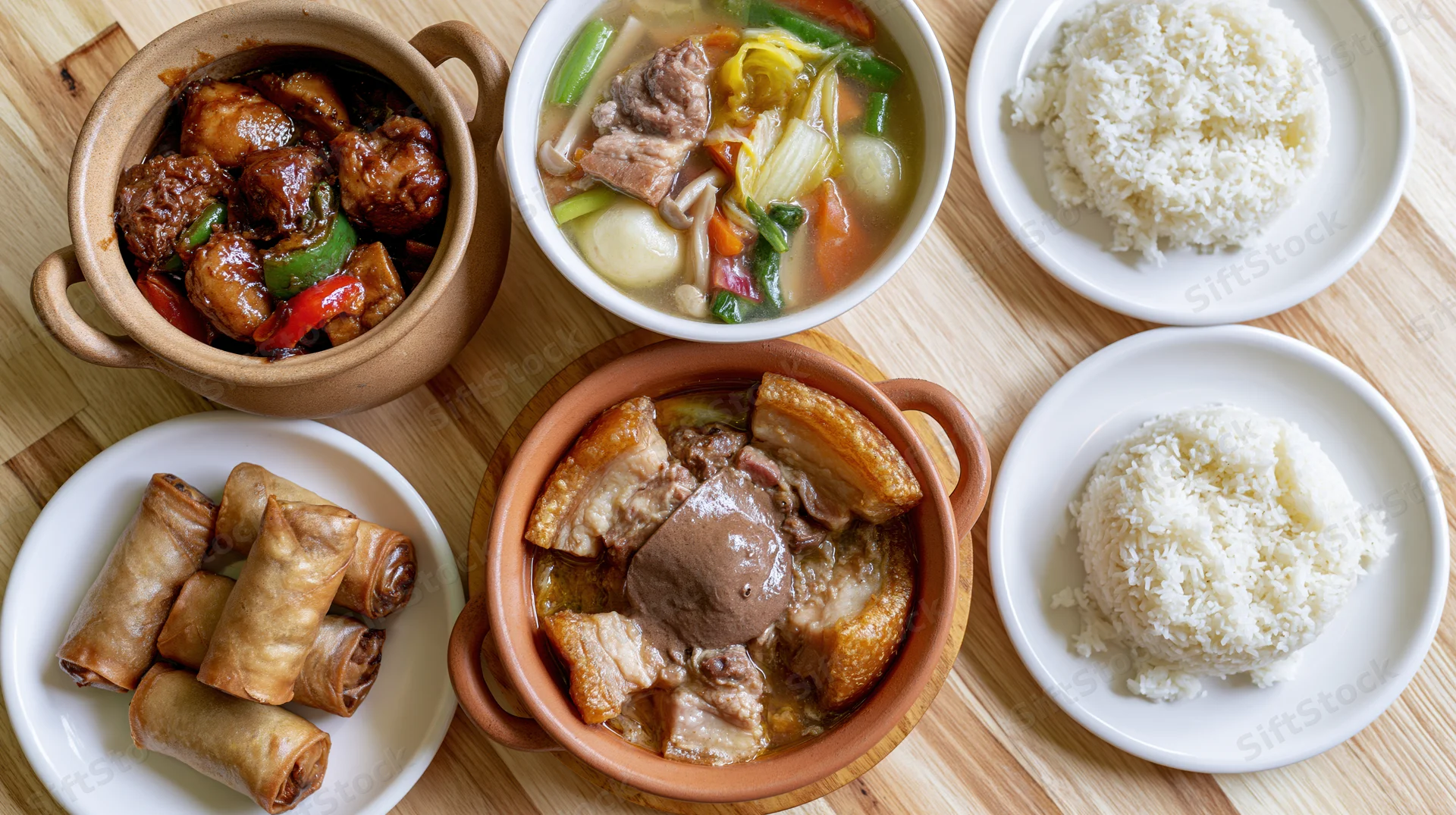 Overhead flat-lay of a filipino home-cooked meal spread on a wooden table with clay pots and white plates containing adobo, sinigang, lumpia, and rice