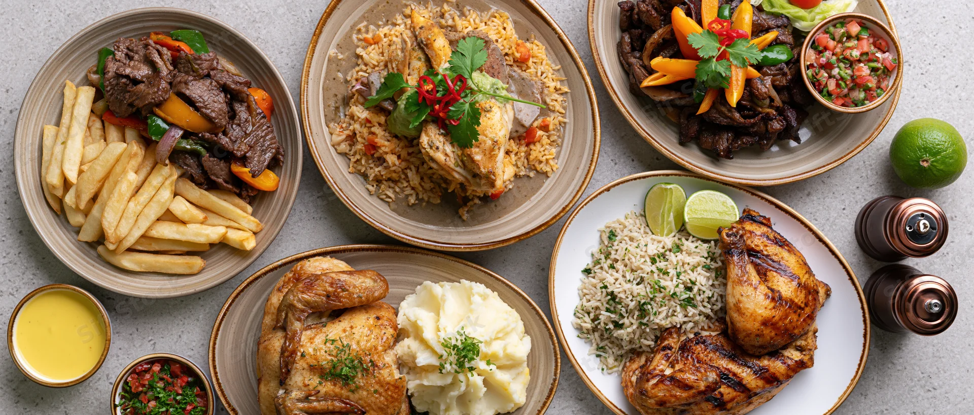 Overhead flat-lay of multiple Peruvian dishes arranged on a table including grilled chicken, beef, rice, fries, and sauces