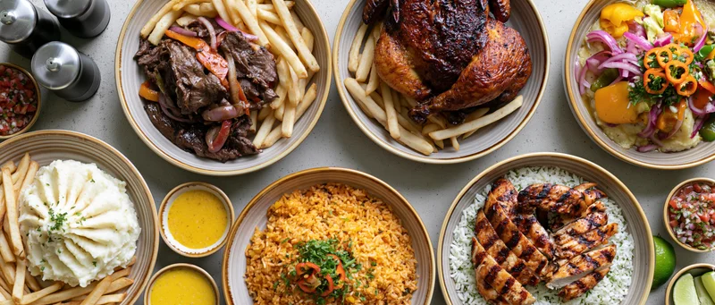 Overhead flat-lay of multiple peruvian dishes served on a table with rice, fries, grilled meats, and sauces