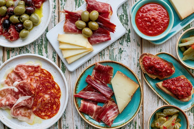 Spanish tapas spread with cured meats, cheese, olives and bruschetta arranged on a rustic wooden table in overhead flat lay