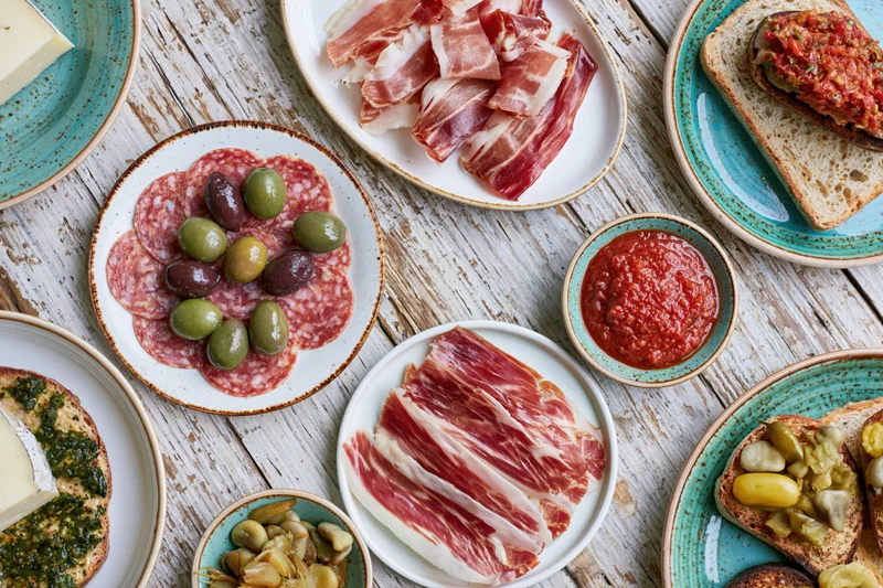 Spanish tapas spread with bacon, salami, olives, cheese and bread on a rustic wooden table