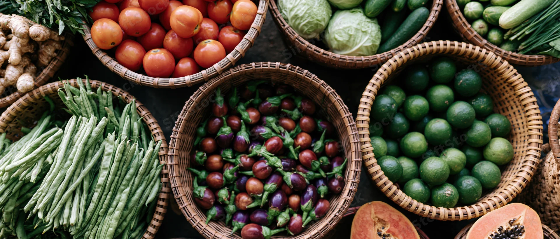 Overhead view of woven baskets filled with fresh vegetables and fruits arranged on a market stall