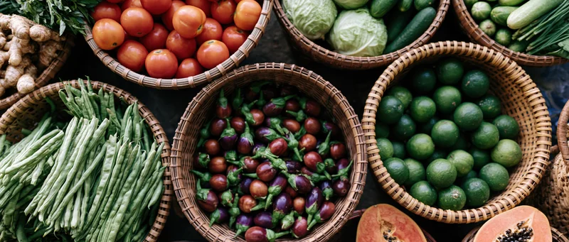Overhead view of woven baskets filled with fresh vegetables and fruits arranged on a market stall